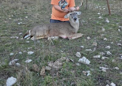 Our grandson with a deer he hunted in a grassy outdoor area with trees in the background.
